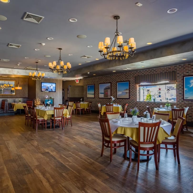 An empty Davinci's Italian restaurant dining room with tables set, chandeliers, and brick walls.