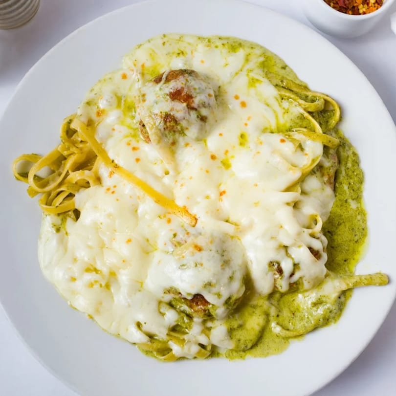 Davinci's pesto pasta with meatballs and melted mozzarella cheese on a white plate.
