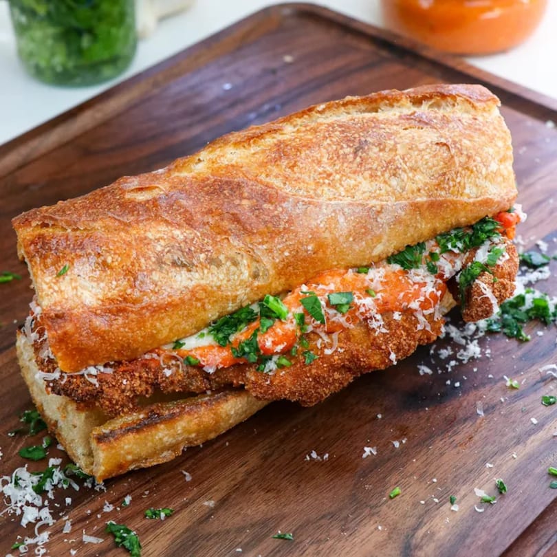 Davinci's chicken parmesan sandwich on a wooden board, topped with sauce, cheese, and parsley.